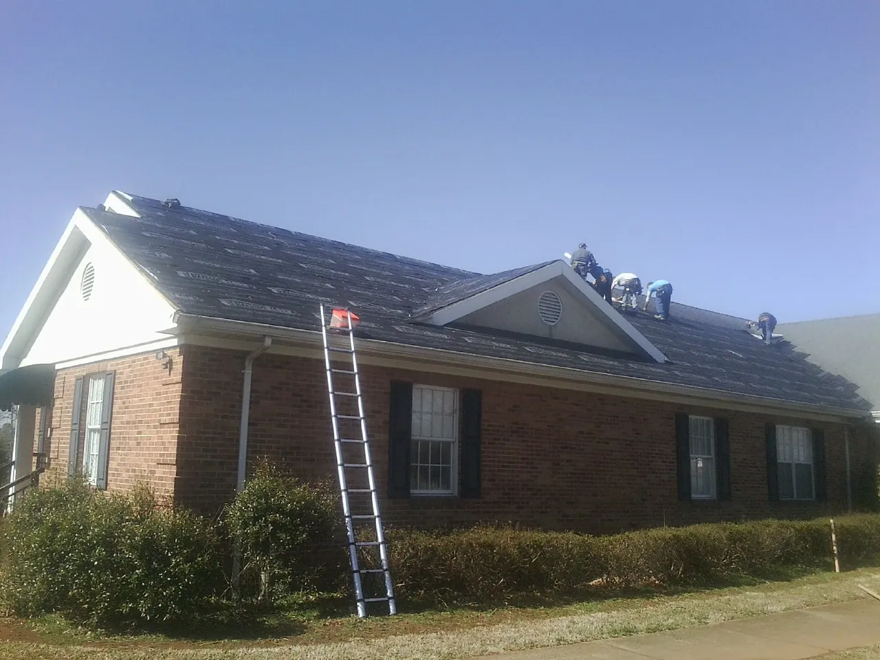 Crew tearing shingles off a brick ranch roof with a ladder set — Metal Roof Repair work by our crew in Wallingford