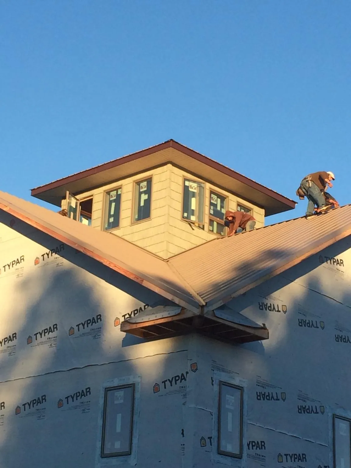 Roofers working around a rooftop cupola on a new metal roof at sunset — Roof Waterproofing in Wallingford by Roofing Brothers